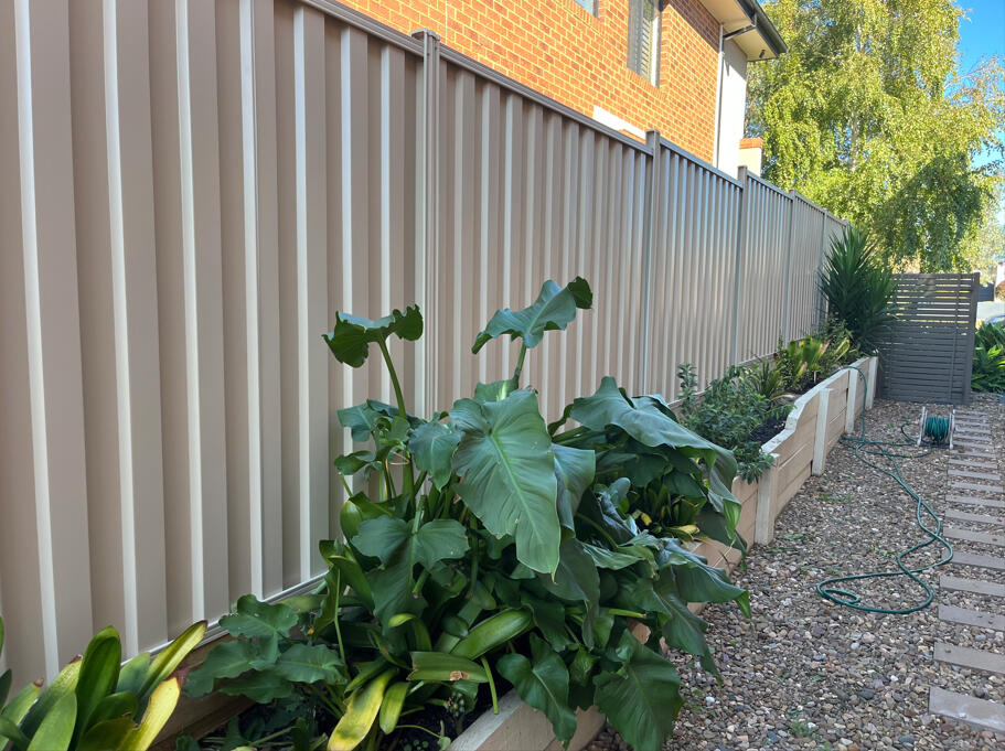 Paperbark Colorbond fence with timber sleepers and stepped panels installed on sloping ground in Berwick 2m high Colorbond privacy fence with timber sleepers and stepped panel design completed for a shared boundary on a sloping block in Berwick.