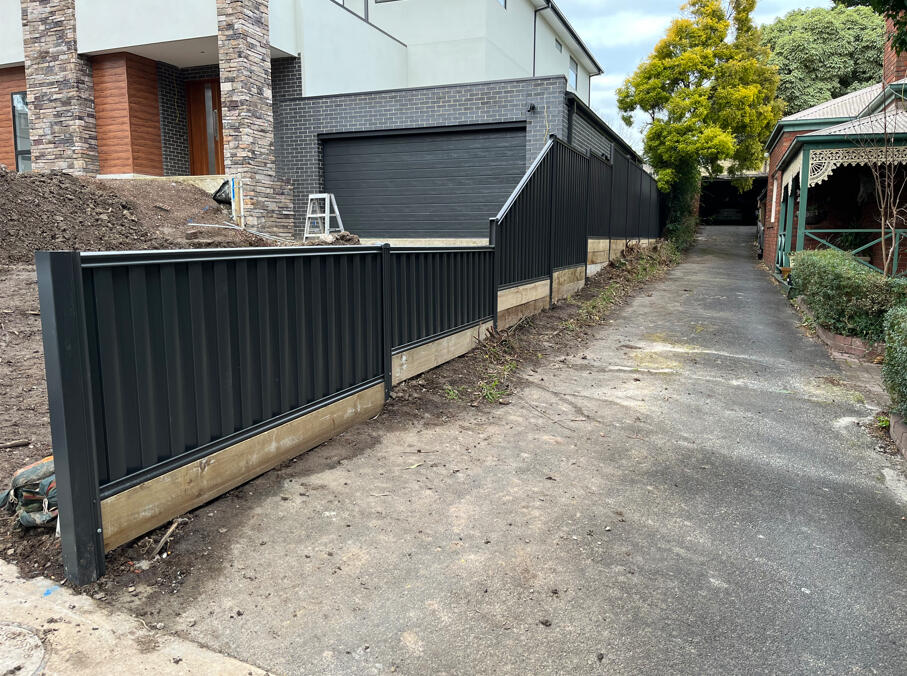 Monument Colorbond fencing with multiple aluminium sleepers and stepped panels installed on steep ground. Monument Colorbond fence with stepped panel design and multiple sleepers installed on a steep sloping block in Berwick.