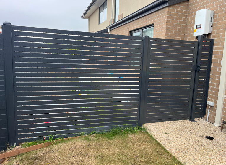 Black aluminium slat pedestrian gate with matching side privacy fence and 10mm slat spacing. Modern black aluminium slat side gate and privacy screen fencing completed in Noble Park North to upgrade existing Colorbond fencing with a more architectural look.