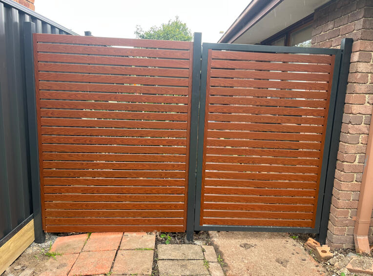 Custom automated aluminium slat driveway gate completed in Narre Warren South featuring Monument frame, timber-look slats, 10mm spacing and remote-controlled motor system.