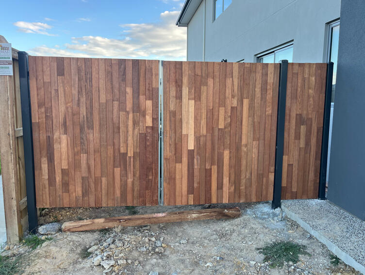 Custom Merbau double driveway gates with powder-coated Monument steel frame completed in Officer to complement existing timber fencing and provide secure side property access.